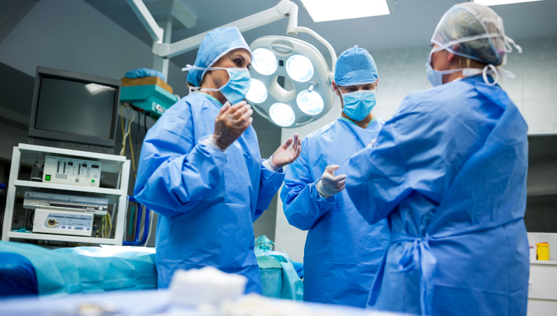 Três cirurgiões conversando uniformizados dentro de um bloco cirúrgico. Imagem ilustrativa para o artigo sobre